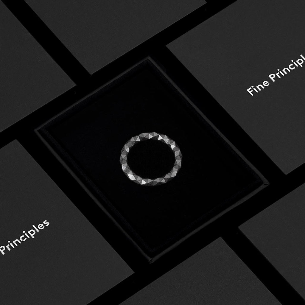 Ring XFRI2562 mit 128 Facetten und mit grafischem Anspruch, handgefertigt aus recyceltem Edelmetall — nachhaltiger Schmuck von Fine Principles Berlin, elegant inszeniert in schwarzer Box.