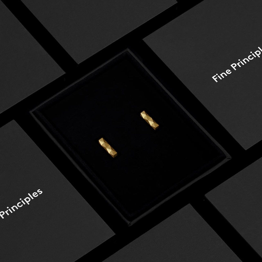 Kleine Stabohrringe XFBE322S von Fine Principles aus Berlin — nachhaltiger Schmuck aus recyceltem 935 Silber oder 750 Gold mit 32 unpolierten Facetten, präsentiert im schwarzen Schmucketui.