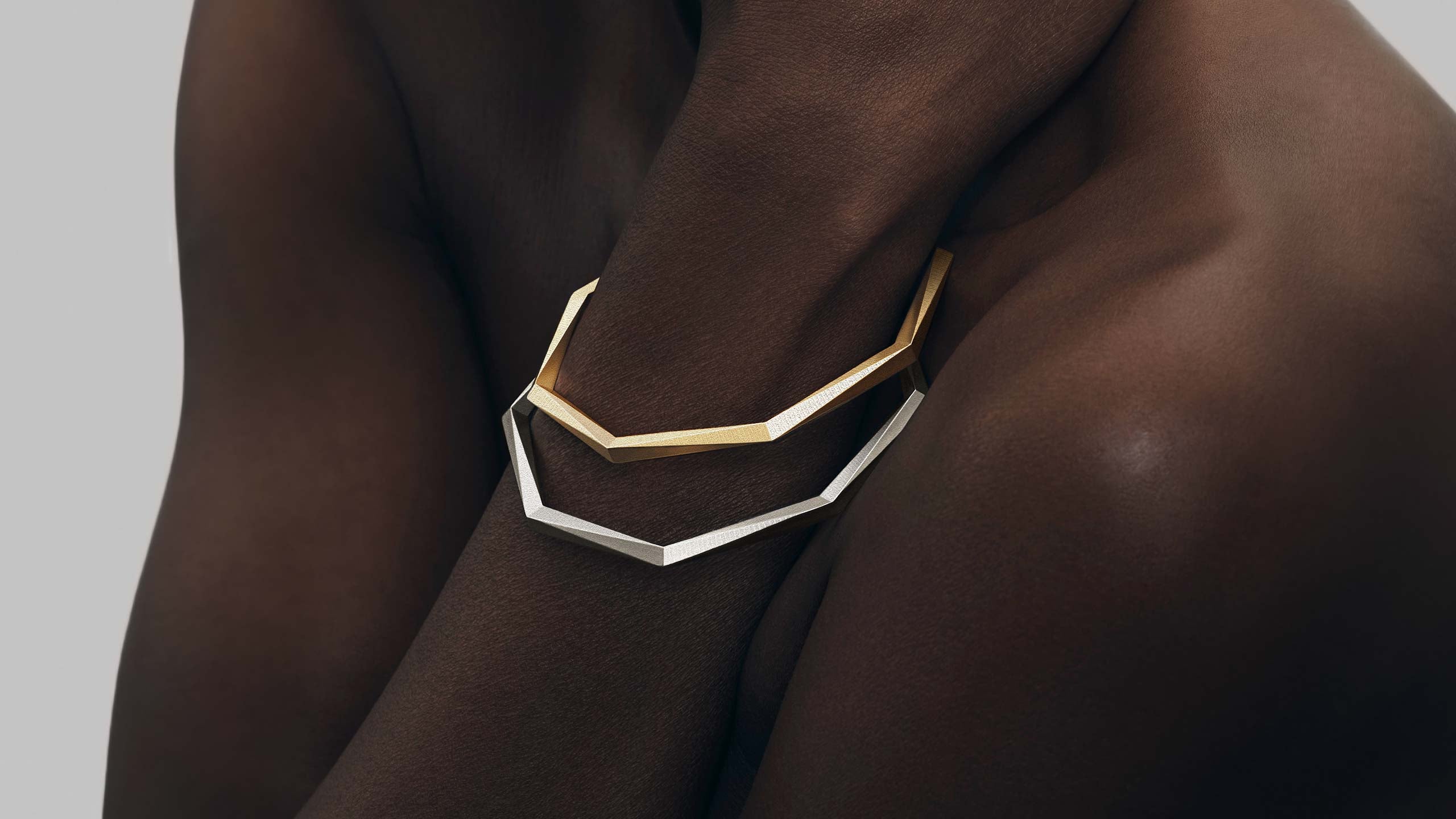 Minimalistische Armreifen mit 64 Facetten aus recyceltem 935 Silber und 750 Gold — nachhaltiger Schmuck von Fine Principles, stilvoll im Duett am Arm getragen.